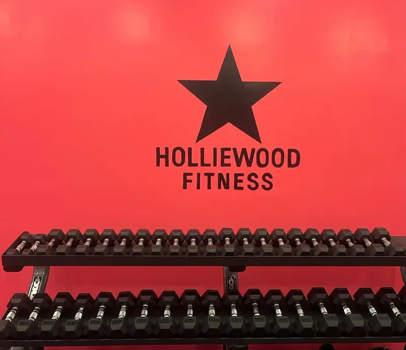 Dumbbell rack in front of the Holliewood Fitness logo wall